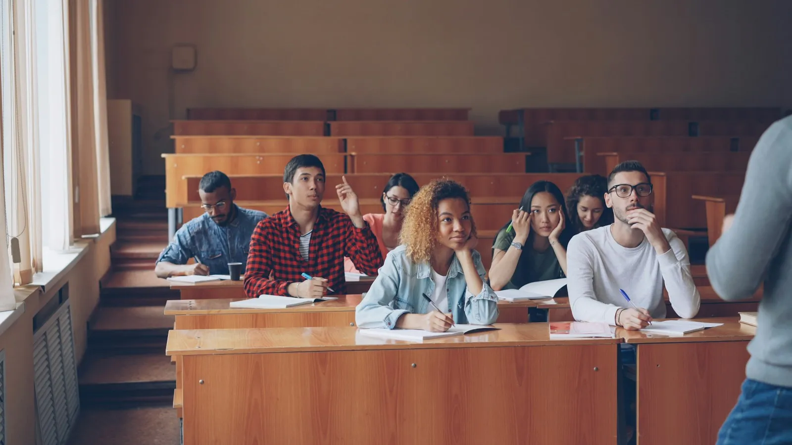 Adult students raising their hands in a university lecture hall